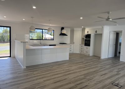 Bright white kitchen with a large island, pendant lights, and a ceiling fan in a modern open-plan space.