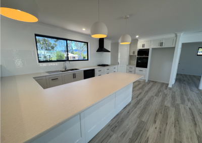 Bright modern kitchen with a long white island, white cabinets, and stainless appliances under three pendant lights.